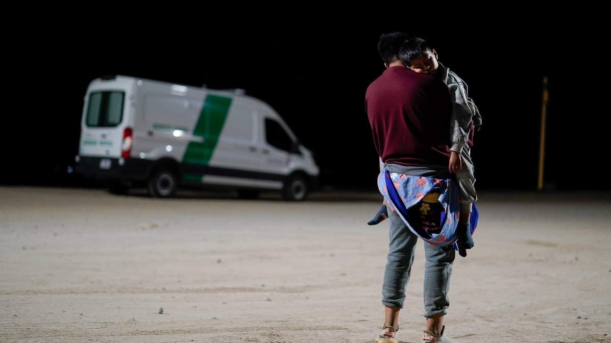 Un hombre colombiano carga a su hijo mientras espera a solicitar asilo después de cruzar la frontera desde México