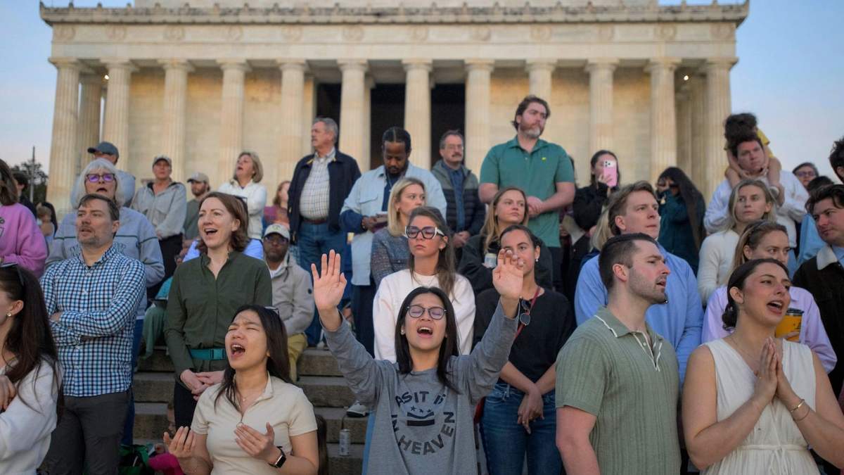 Gente levanta las manos al cielo en canto durante un servicio de oración al amanecer del Domingo de Pascua en el Lincoln Memorial
