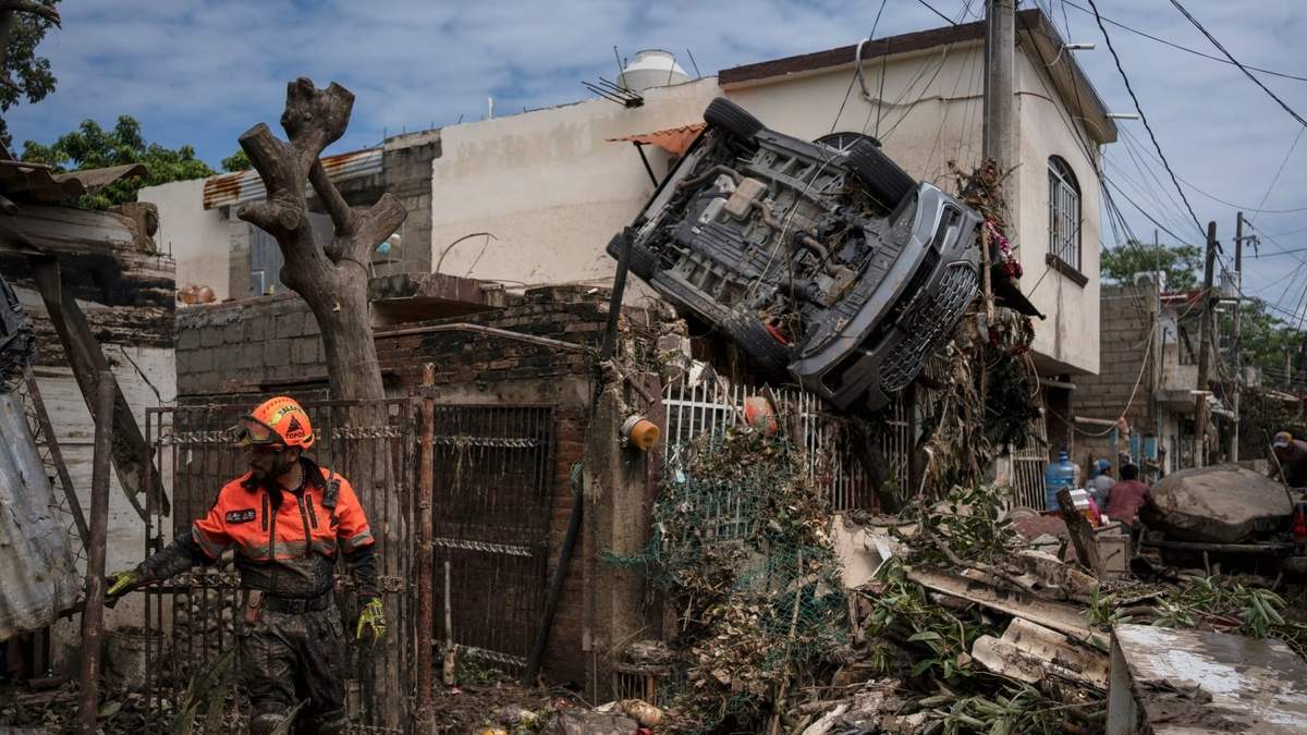 Un rescatista de la brigada de voluntarios Topos trabaja cerca de un automóvil colgado de una cerca junto a una casa dañada en Poza Rica