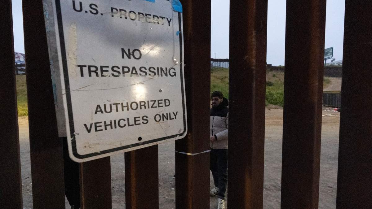 Migrantes esperan entre las vallas fronterizas que separan a Tijuana de San Diego para solicitar asilo a las autoridades estadunidenses