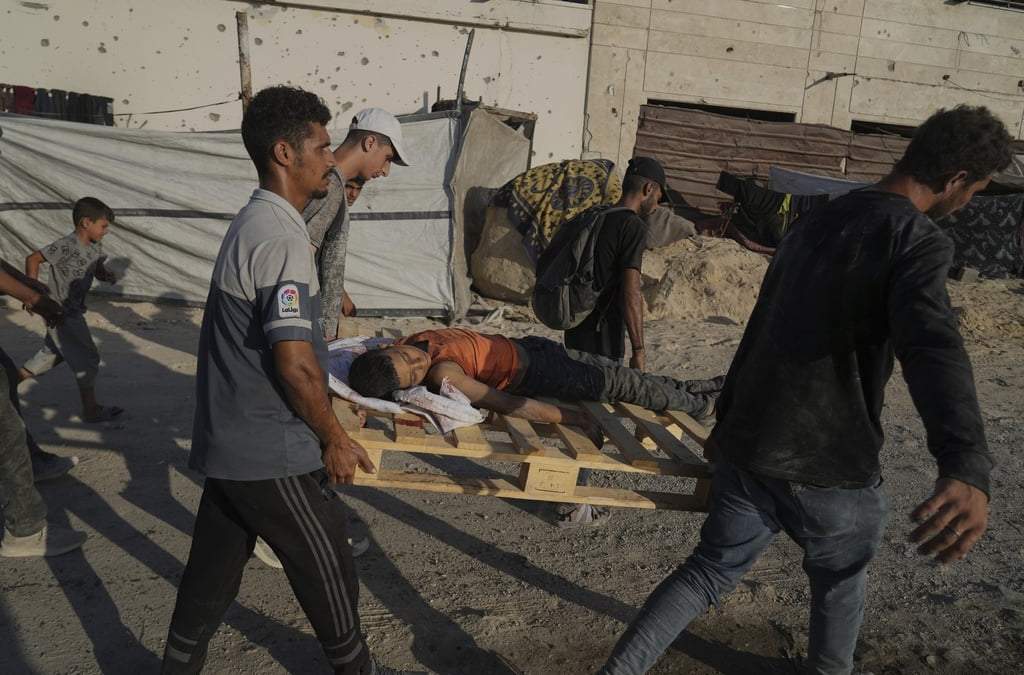 Palestinos llevan el cuerpo de un niño que murió mientras intentaba llegar a un convoy de ayuda humanitaria en las afueras de Beit Lahiya, mientras caminan por una carretera en la ciudad de Gaza, en la Franja de Gaza, el domingo 24 de agosto de 2025