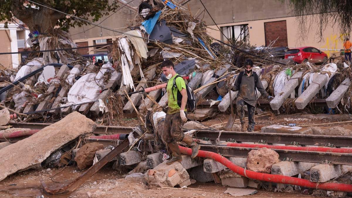 Voluntarios cruzan una vía del tren tras las inundaciones en Paiporta, España