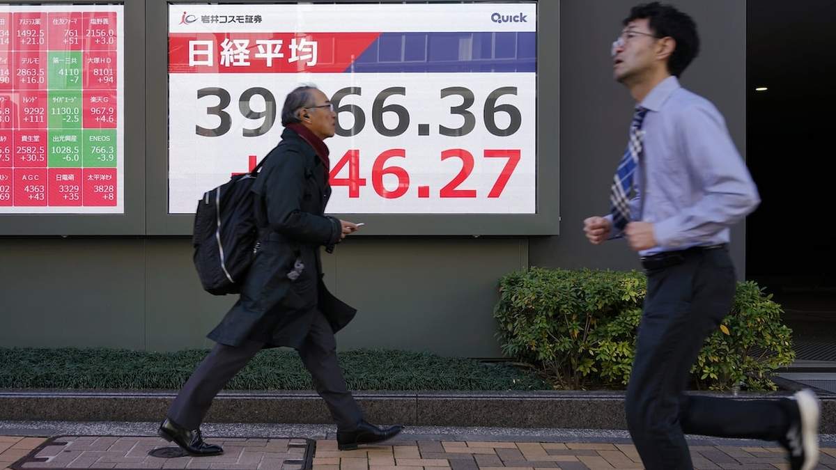 Dos personas pasan por delante de una pantalla que muestra la cotización en el índice Nikkei de Japón este martes