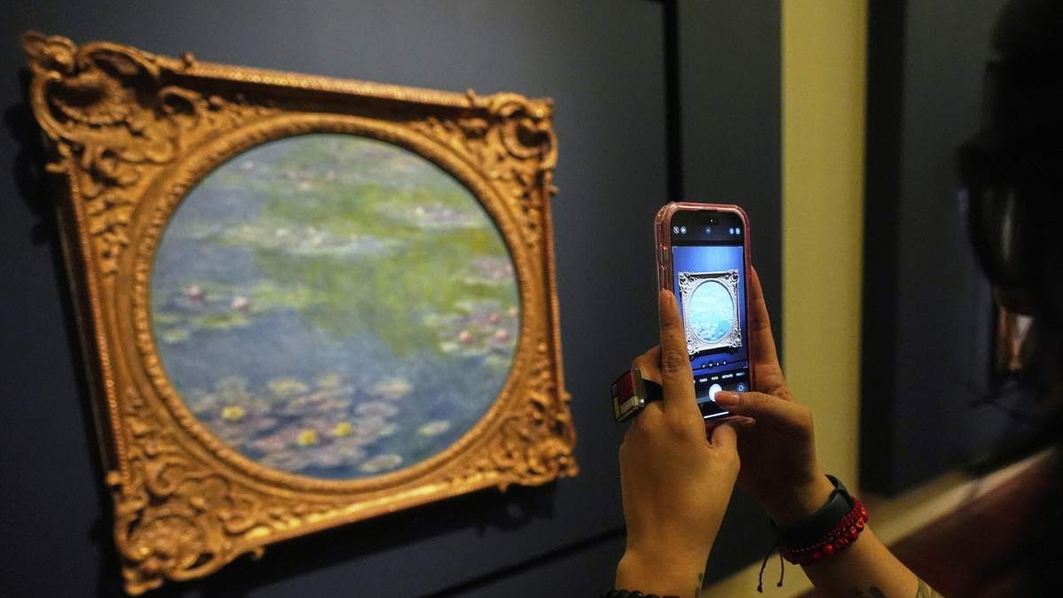 Un visitante toma fotografías de una pintura de Claude Monet durante una gira de prensa de la exposición: La Revolución Impresionista, en el Palacio de Bellas Artes en la Ciudad de México