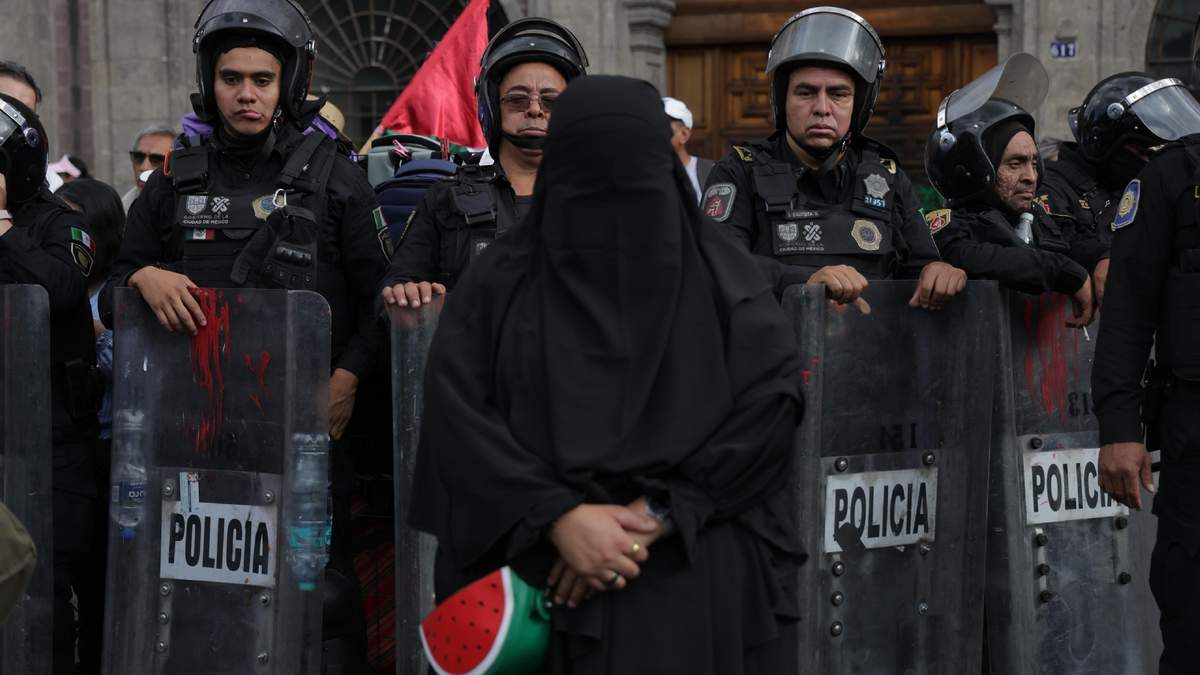 Una persona encapuchada se para frente a los policías durante la protesta
