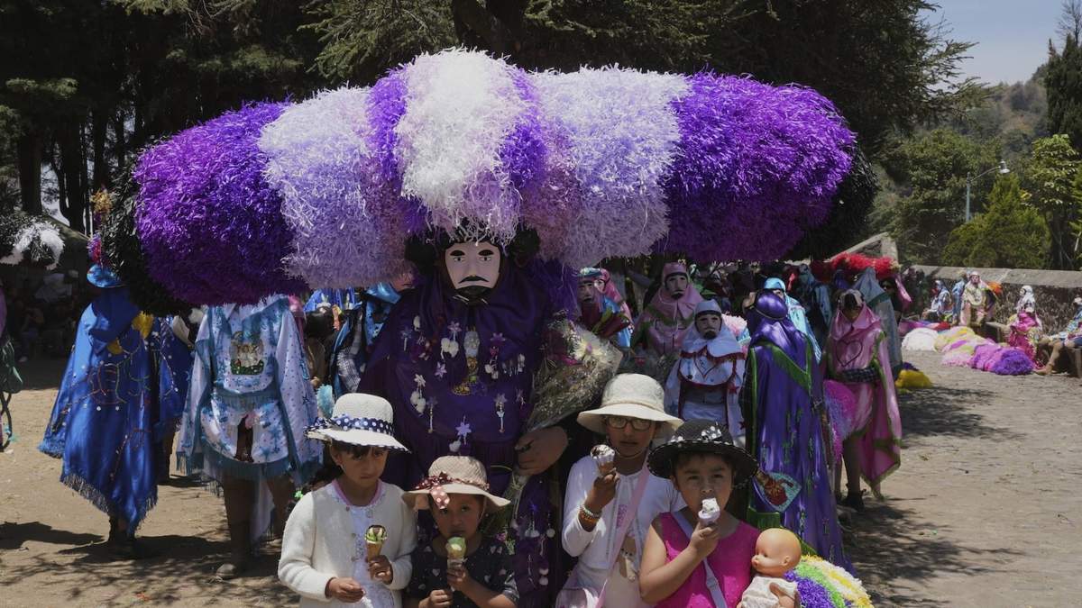 Niños posan para una fotografía frente a un personaje llamado "sayón", el cual tiene un sombrero hecho con pañuelos de papel, durante los festejos de Pascua en Tetela del Volcán