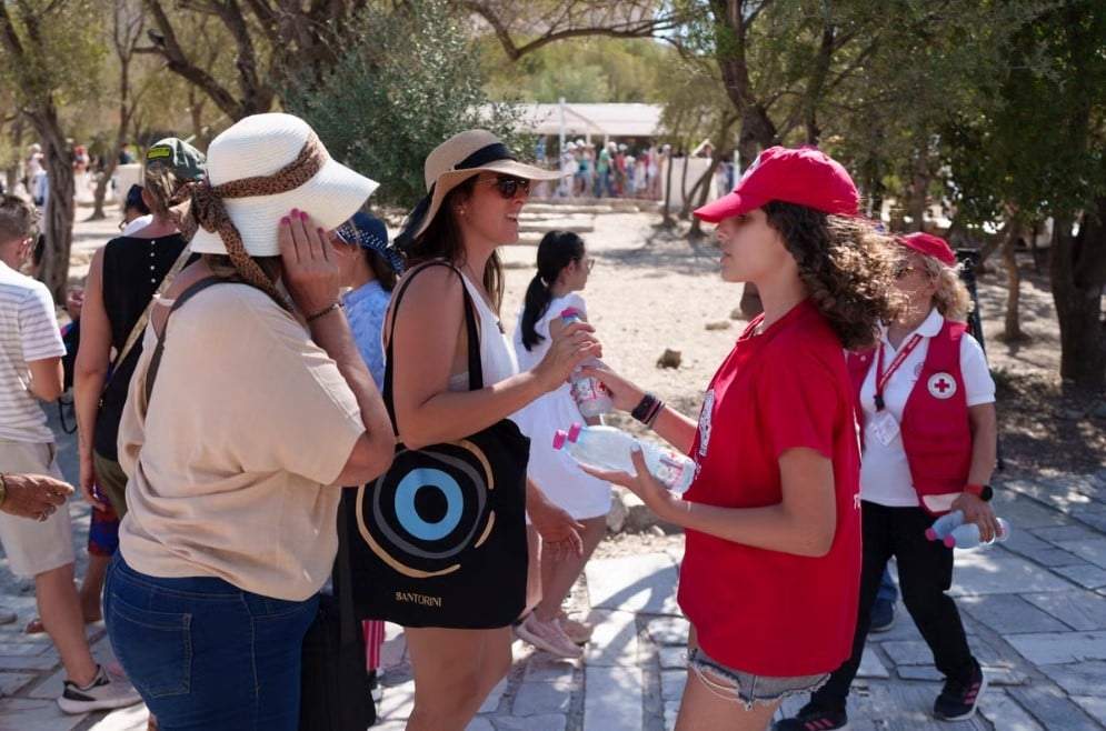 Una voluntaria de la Cruz Roja entrega botellas de agua fría a turistas en la Acrópolis durante un caluroso día en Atenas