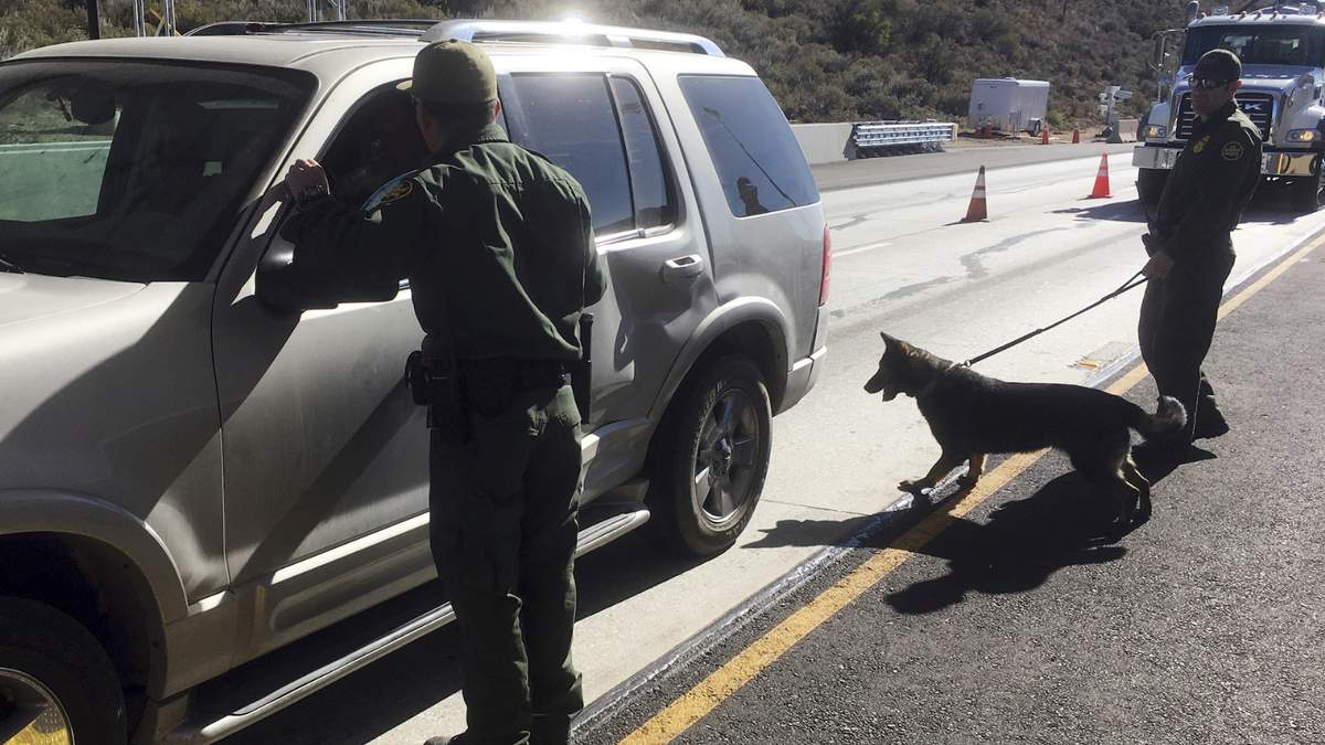 Agentes de la Patrulla Fronteriza se apoyan en un elemento canino en la revisión vehicular en un punto de revisión de Pine Valley, California