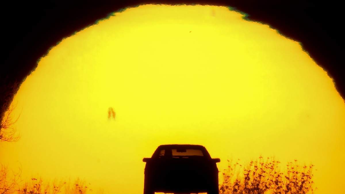 Un vehículo avanza contra la puesta de sol en el solsticio de verano