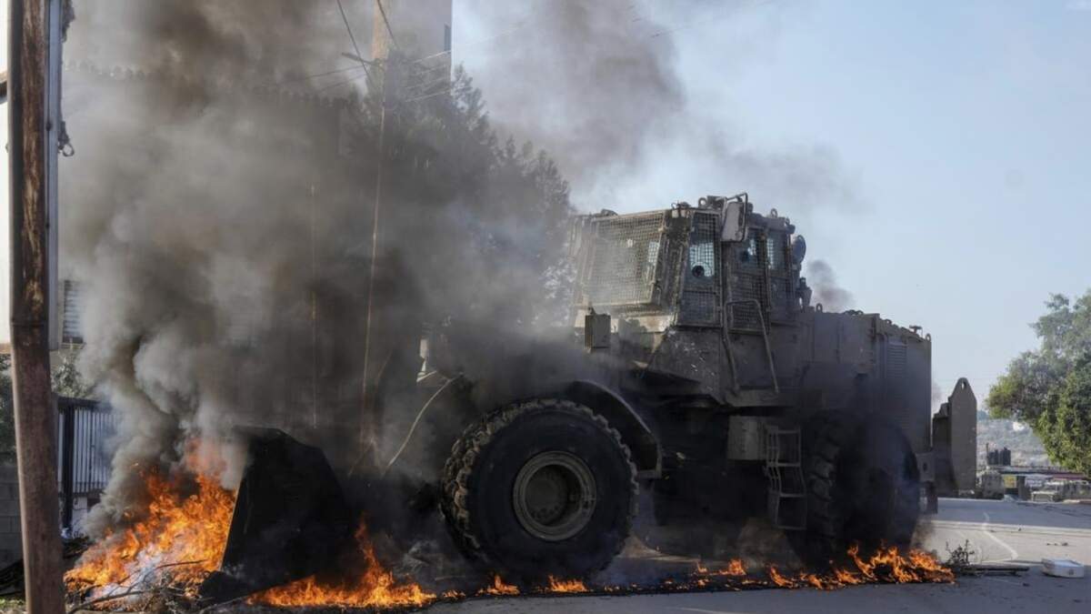 Un vehículo militar israelí retira neumáticos en llamas que bloquean una carretera durante una incursión del ejército en el campo de refugiados de Faraa, en Cisjordania