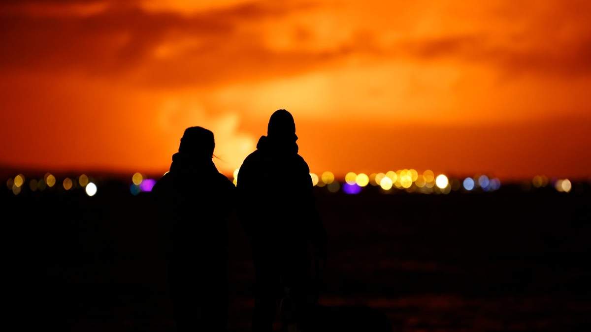 Personas observan el cielo nocturno iluminado por la erupción de un volcán en la península de Reykjanes, en Islandia