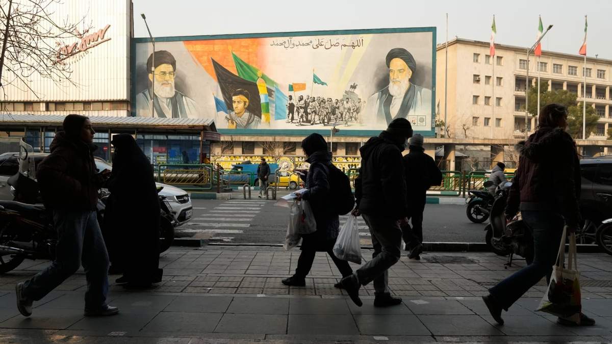 La gente camina frente a un mural que representa al difunto fundador revolucionario iraní, el ayatolá Jomeini, en Teherán, Irán