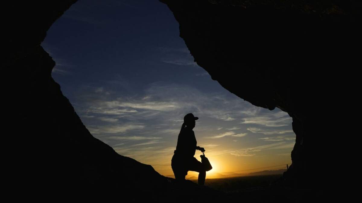 Un senderista pasa frente a la caverna Hole-in-the-Rock de Papago Park al amanecer, Phoenix
