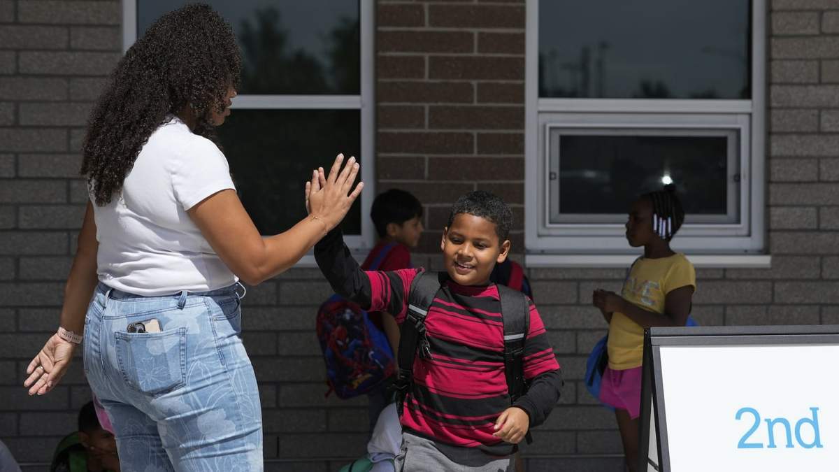 Dylan Martínez-Ramírez, centro, saluda a su maestra Aliah James, izquierda, en su escuela en Aurora, Colorado, el 29 de agosto