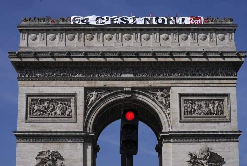 Sindicalistas despliegan una pancarta con la leyenda "64 es no" en lo alto del Arco de Triunfo, París, miércoles 5 de abril de 2023