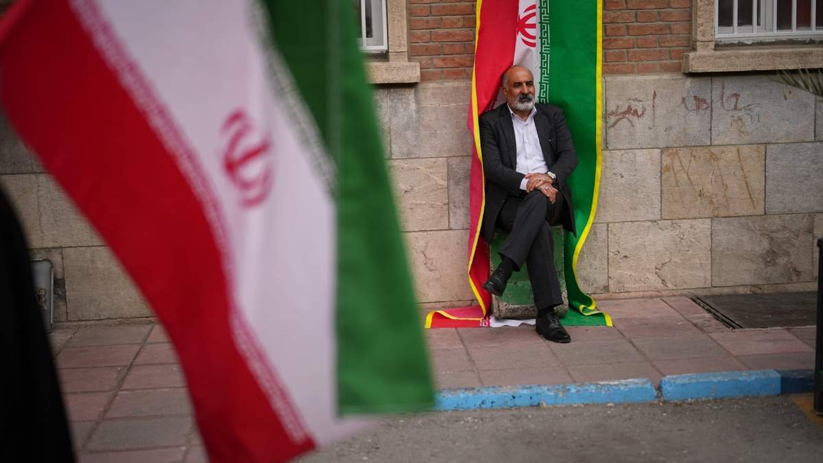 Un hombre se sienta junto a una pancarta con la bandera iraní durante una protesta patrocinada por el gobierno, a la que asistieron trabajadores de la salud, contra la campaña militar estadounidense-israelí