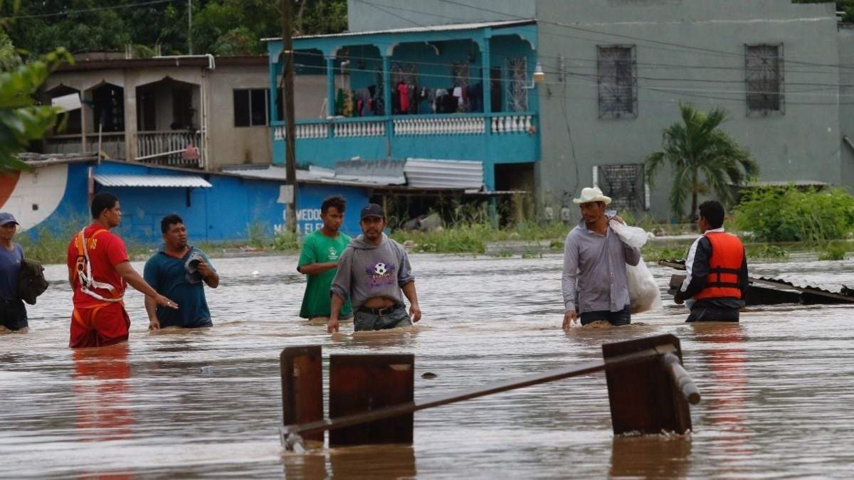 Hombres caminan por una calle inundada después del paso del huracán "Iota" en La Lima, Honduras