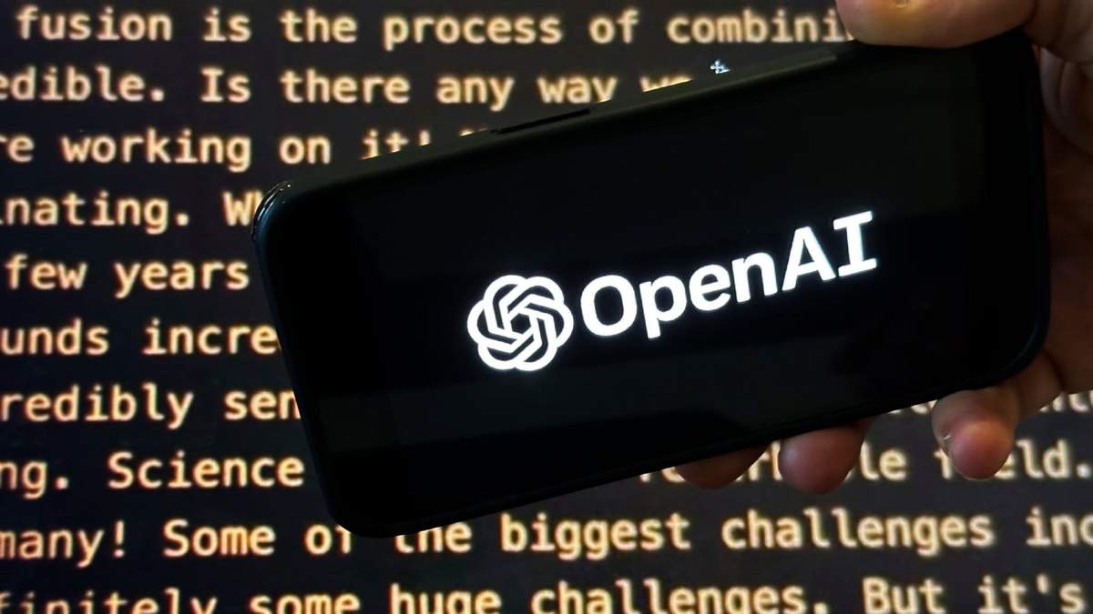 El logo de OpenAI en un teléfono celular frente a una pantalla que muestra el website de la compañía